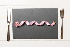 Healthy diet concept of plate with measuring tape, fork and knife on wooden background. Top view photo