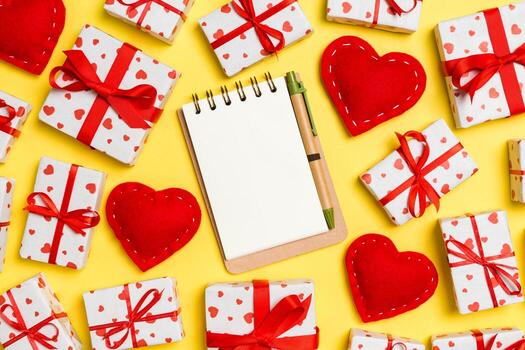 Holiday composition of notebook, gift boxes and red textile hearts on colorful background with empty space for your design. Top view of Valentine's Day concept photo