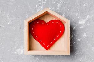 vista superior del corazón textil rojo en una casa de madera sobre fondo de cemento. concepto de hogar dulce hogar. día de San Valentín foto