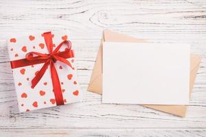 correo de sobre con corazón rojo y caja de regalo sobre fondo blanco de madera. tarjeta de san valentín, amor o concepto de saludo de boda foto