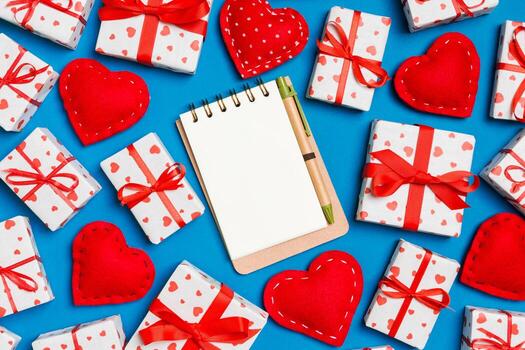 Holiday composition of notebook, gift boxes and red textile hearts on colorful background with empty space for your design. Top view of Valentine's Day concept photo
