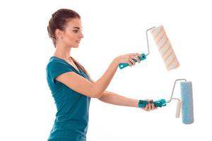 beautiful young brunette builder girl in uniform makes renovation with paint rollers in her hands isolated on white background photo