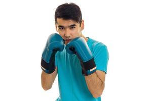 retrato de un joven deportista de pelo oscuro practicando boxeo con guantes azules y uniforme aislado de fondo blanco foto