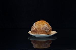 hogaza redonda de pan de masa fermentada artesanal casero recién horneado en un plato de cerámica. fondo negro puro. es genial para el cartel de promoción de panadería. foto