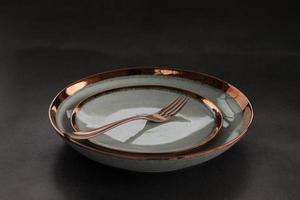 tenedor de metal sobre plato de cerámica de lujo, color oro rosa. fondo oscuro foto