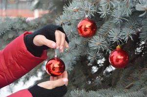 The girl hangs a red ball on the Christmas tree. Christmas decorations. Holiday. photo