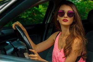 Young beautiful brunette sits by the driving wheel in a car photo