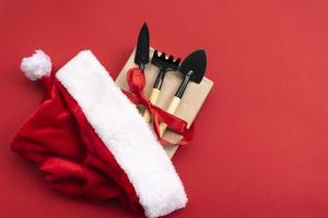 Christmas and new year composition with garden tools, shovel and rake and Santa Claus hat on a red background. The concept of gardening and farming for cards, calendars, covers. photo