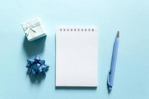 Notebook and pen on a blue background, spiral notepad with gift on a table. space for your text, greetings, top view. photo