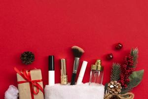 Flat lay composition with makeup products and Christmas decor on red paper background. Xmas, happy new year 2021, female wishes concept. photo