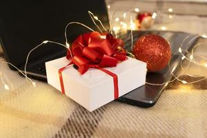 caja de regalo blanca con lazo rojo y portátil con luz navideña foto
