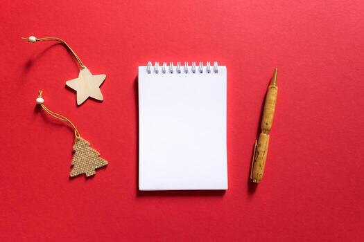 cuaderno y bolígrafo sobre un fondo rojo, bloc de notas en espiral con árbol de navidad y estrella sobre una mesa. espacio para su texto, saludos, vista superior. foto