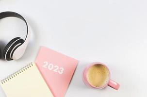 flat lay of blank paper note book on pink diary 2023, headphones and pink cup of coffee on white background. photo