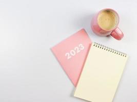 flat lay of blank paper note book on pink diary 2023 and pink cup of coffee on white background. photo