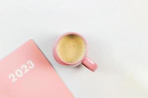 flat lay of pink 2023 diary or planner with pink cup of coffee on white background. New year plans or resolutions concept. photo