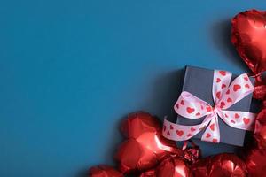 caja de regalo y globos con forma de corazón rojo sobre fondo azul. tarjeta de felicitación del día de san valentín. copie el espacio