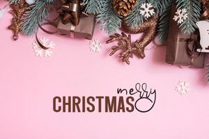 Merry Christmas greeting text and pine trees branches with xmas New Year decoration top view, flat lay on pink background photo