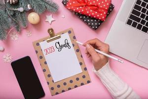 2023 goals female hand write and Cristmas New Year work table decoration top view, flat lay on pink background photo