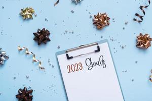 2023 goals text on tablet and bright festive background with bows and beads top view. Motivation new year plans writing photo