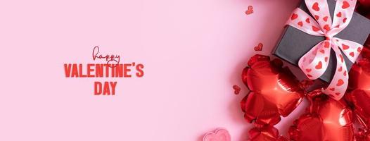 feliz día de san valentín texto en la tarjeta de felicitación. banner con caja de regalo con lazo y globos en forma de corazón sobre fondo rosa foto