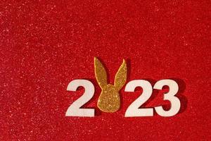 Wooden numbers 2023 with rabbit ears symbol new year on a colored background photo