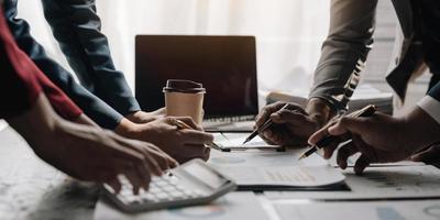 gente de negocios reunida usando computadora portátil, calculadora, cuaderno, papel gráfico del mercado de valores para planes de análisis para mejorar la calidad el próximo mes. conferencia discusión concepto corporativo foto