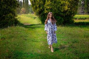 atractiva joven morena vestida con estampado de flores azules camina en el parque grren foto