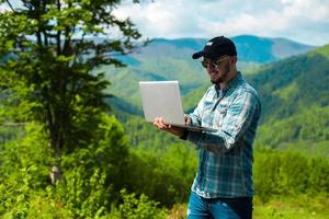 boy smiling and working on laptop in the mountains photo