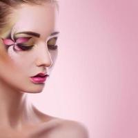 mujer adulta joven con los ojos cerrados y maquillaje creativo sobre fondo rosa foto