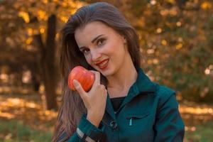 hermosa chica con pintalabios rojo sostiene una manzana en la mano y sonríe de cerca foto