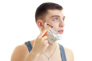 young guy looks away and shaves his beard with a razor close-up