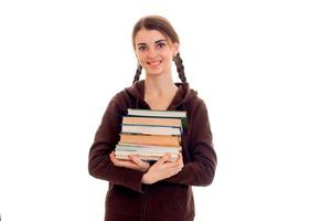 joven estudiante morena feliz con ropa deportiva marrón con coletas y libros en las manos sonriendo a la cámara aislada de fondo blanco foto