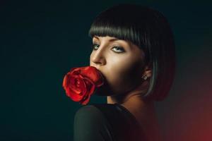 Brunette with green eyes and red rose in mouth photo