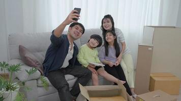 family parent and little daughter and son child sit relax on sofa in living room on new home and take selfie with smartphone together with smiling and cheerful laugh. video