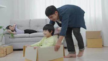 la familia feliz se muda a una nueva habitación en una nueva casa. el hijo se sienta en una caja de cartón y el padre se mueve en una caja y ha sido alentado por la hija y la esposa. mudanza a casa o casa por concepto de familia. video