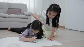 una madre enseña a su hija a dibujar en unas vacaciones familiares. las niñas se están enfocando en dibujar porque es la actividad que más les gusta a las niñas. actividad familiar video