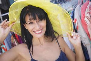 bonita mujer italiana probándose un sombrero amarillo en el mercado foto