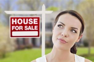 Thinking Woman In Front of House and For Sale Sign photo