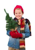 niño usando mitones y bufanda sosteniendo un árbol de navidad en blanco foto