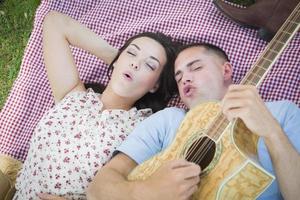 pareja de raza mixta en el parque tocando la guitarra y cantando foto