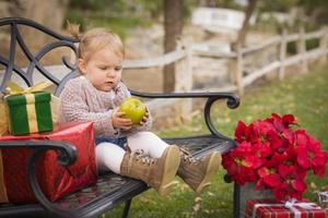 niño pequeño sentado en un banco con regalos de navidad afuera foto