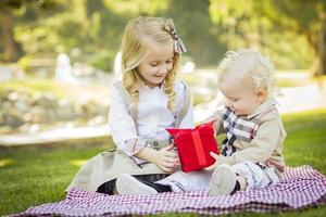 la niña le da un regalo a su hermanito en el parque foto