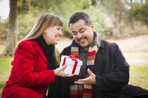 pareja de raza mixta compartiendo regalos de navidad o san valentín afuera foto