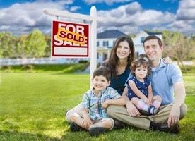 Young Family With Children In Front of Custom Home and Sold For Sale Real Estate Sign. photo