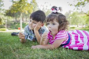 Young Brother and Baby Sister Enjoying Their Lollipops Outdoors photo