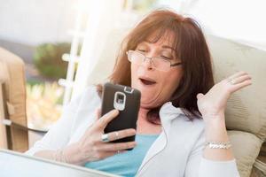 Shocked Middle Aged Woman Gasps While Using Her Smart Phone photo