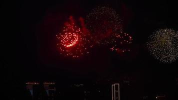 Mehrere Feuerwerkskörper explodierten mit langen Spuren am Nachthimmel. Blitze roter Feuerwerke, die am Nachthimmel über der Stadt kugelförmige Formen erzeugen. video