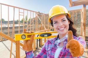 Female Construction Worker with Thumbs Up Holding Level Wearing Gloves, Hard Hat and Protective Goggles at Construction Site photo