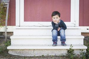 lindo niño de raza mixta sentado en los escalones de un granero foto