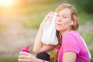 Young Fit Adult Woman Outdoors With Towel and Water Bottle in Workout Clothes Listening To Music with Earphones. photo